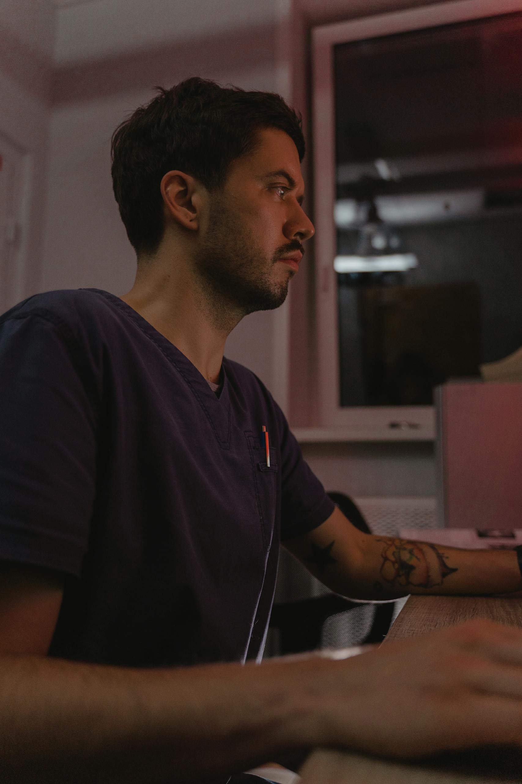 Focused medical professional at desk in evening light, wearing scrub.